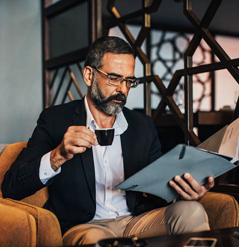 Elegant smart looking Caucasian businessman drinking coffee and reading from papers.